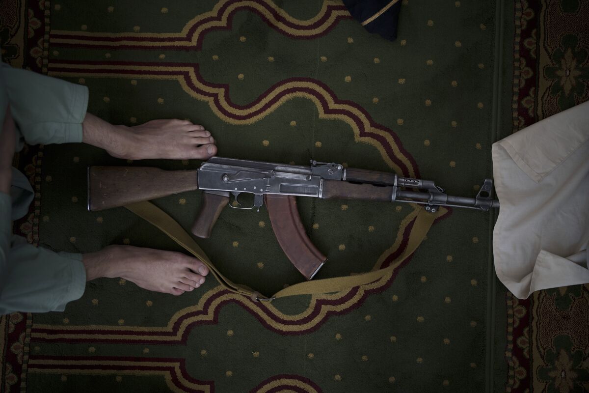 An AK-47 rifle on the floor at someone's bare feet