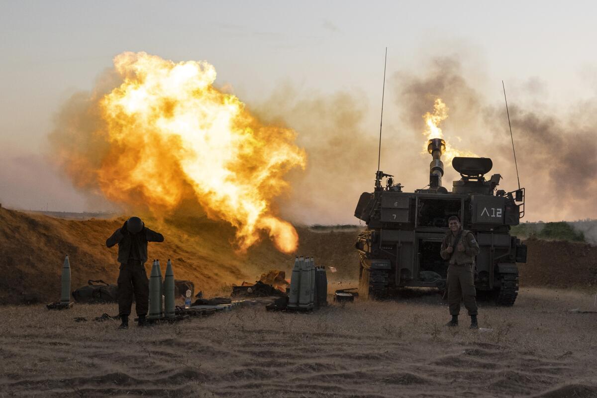 As flames rise to the left, a soldier gives a thumbs-up sign after his artillery unit opens fire