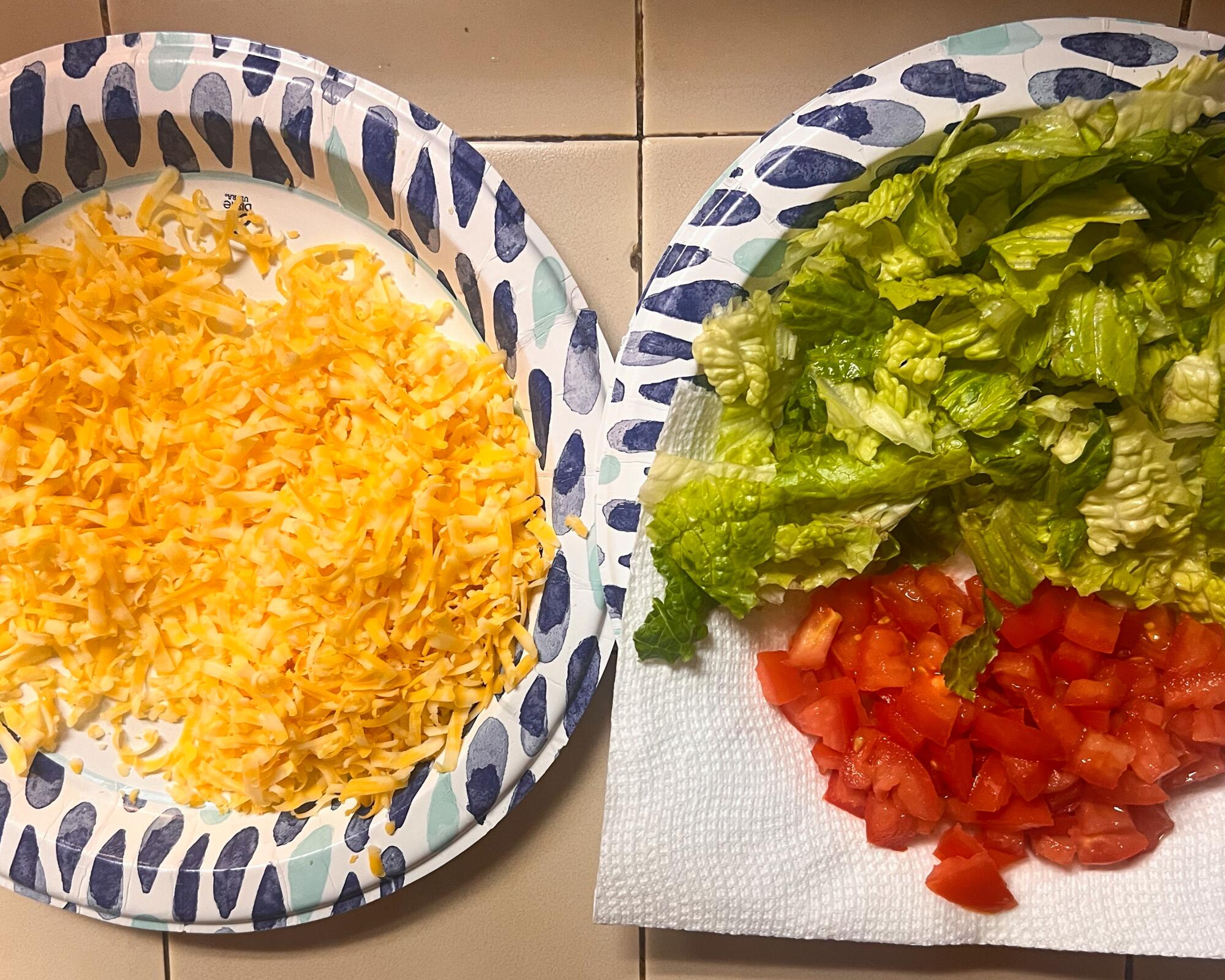 Plates with shredded cheese, lettuce and tomatoes.