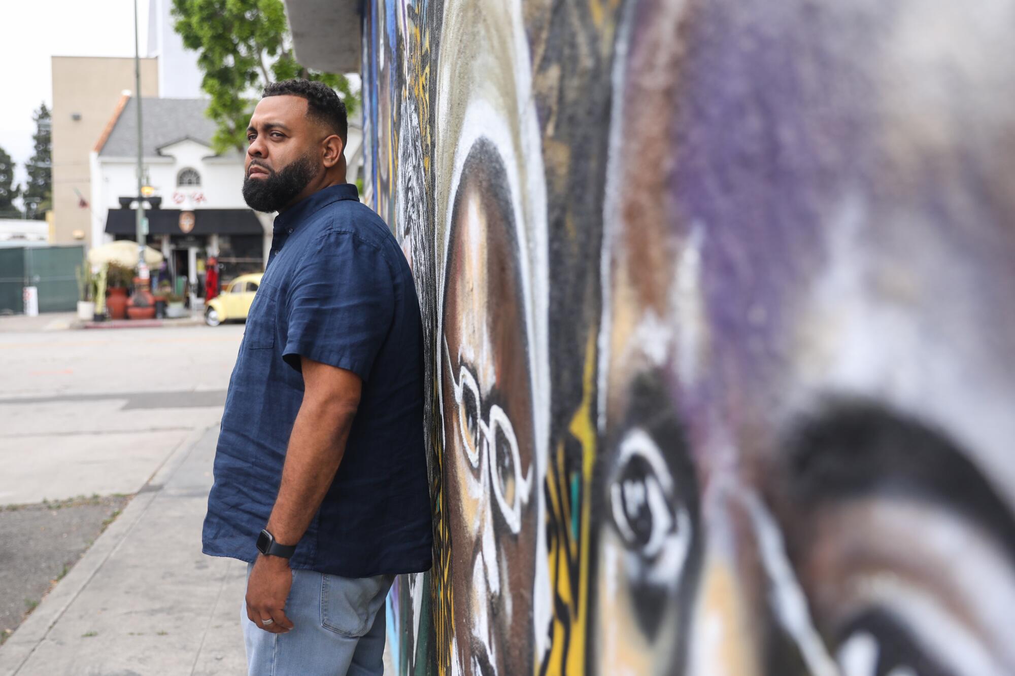 A man stands next to a wall with a mural in Leimert Park.