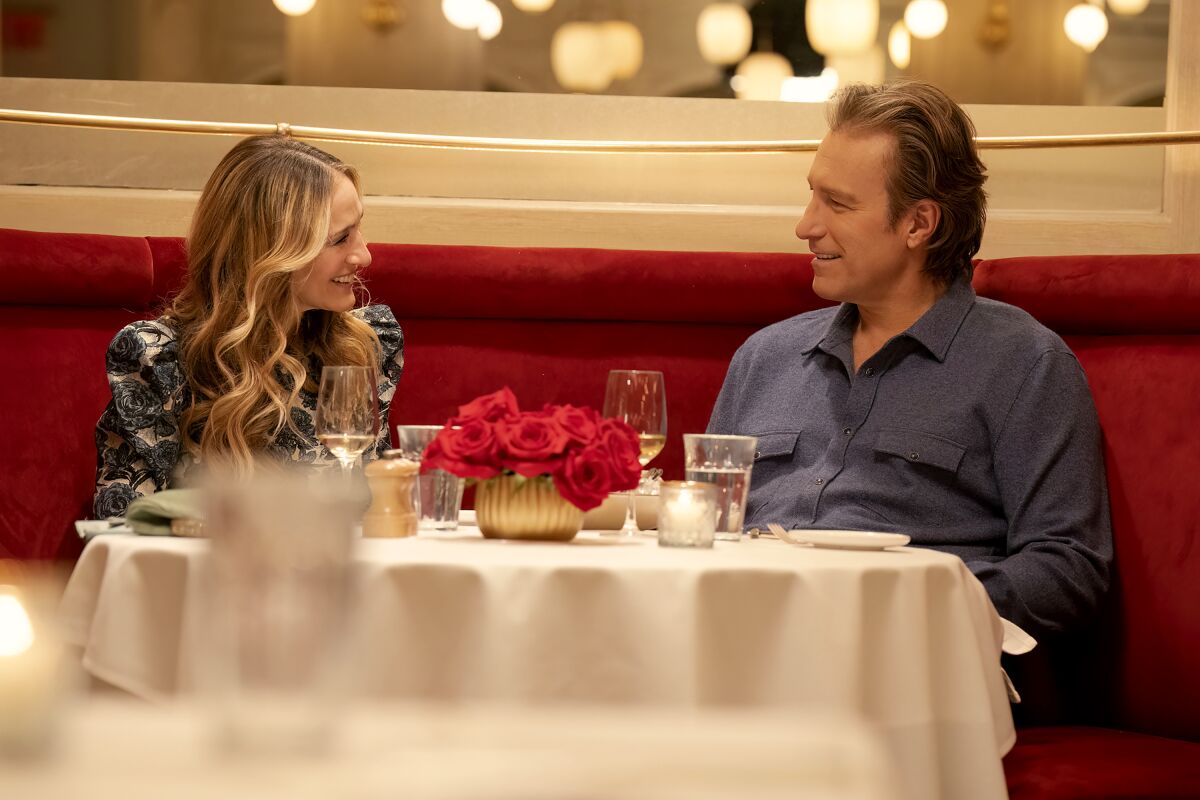 A woman with long hair and a man wearing blue sit at a dining table with roses in the center.