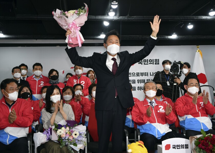 Oh Se-hoon, candidate of the main opposition People Power Party, holds flowers while watching televisions broadcasting the counting for the Seoul mayoral by-election at party headquarters in Seoul, South Korea, Thursday, April 8, 2021. (Song Kyung-Seok/Pool Photo via AP)