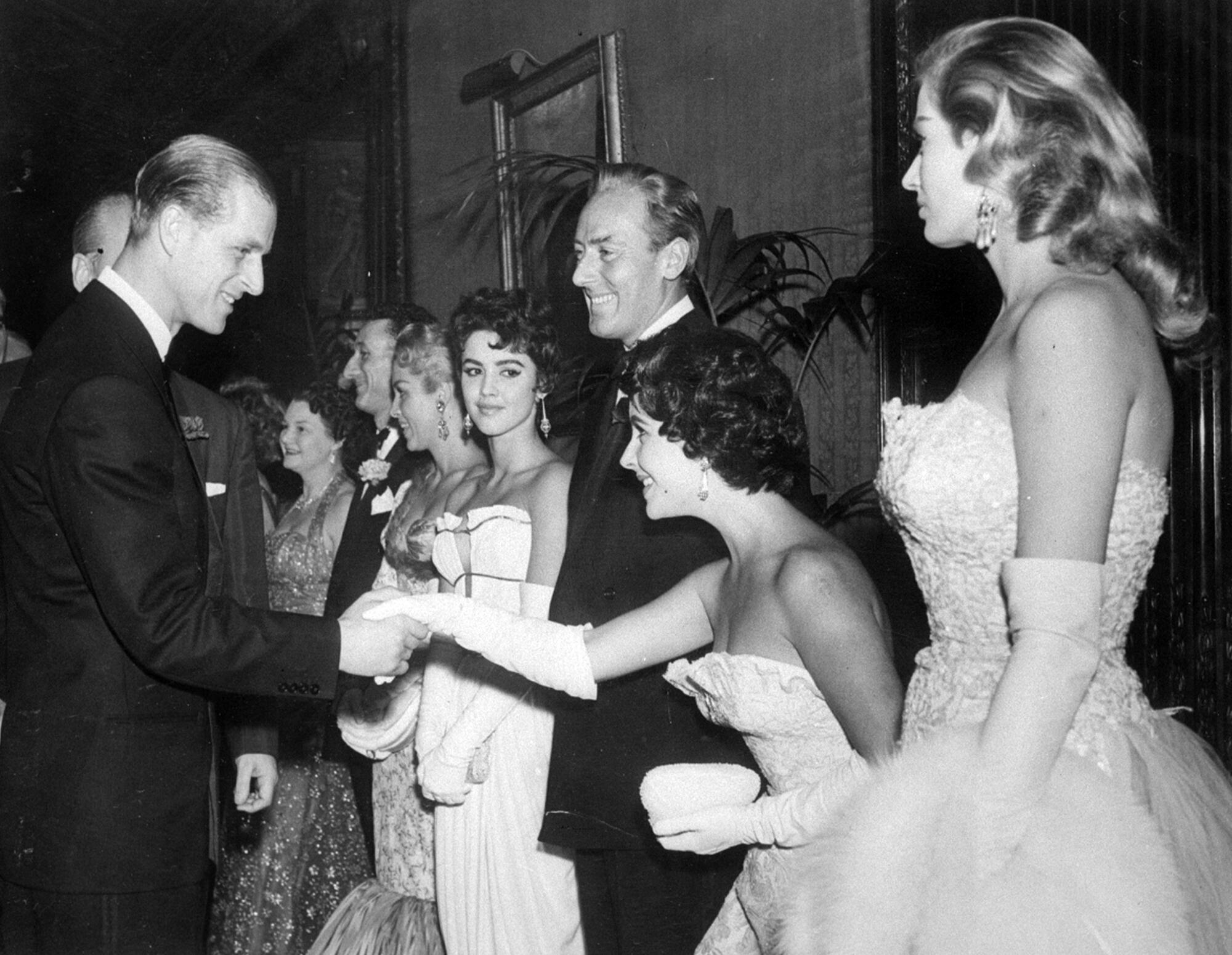 Elizabeth Taylor curtsies in a row of people as Prince Philip greets her.