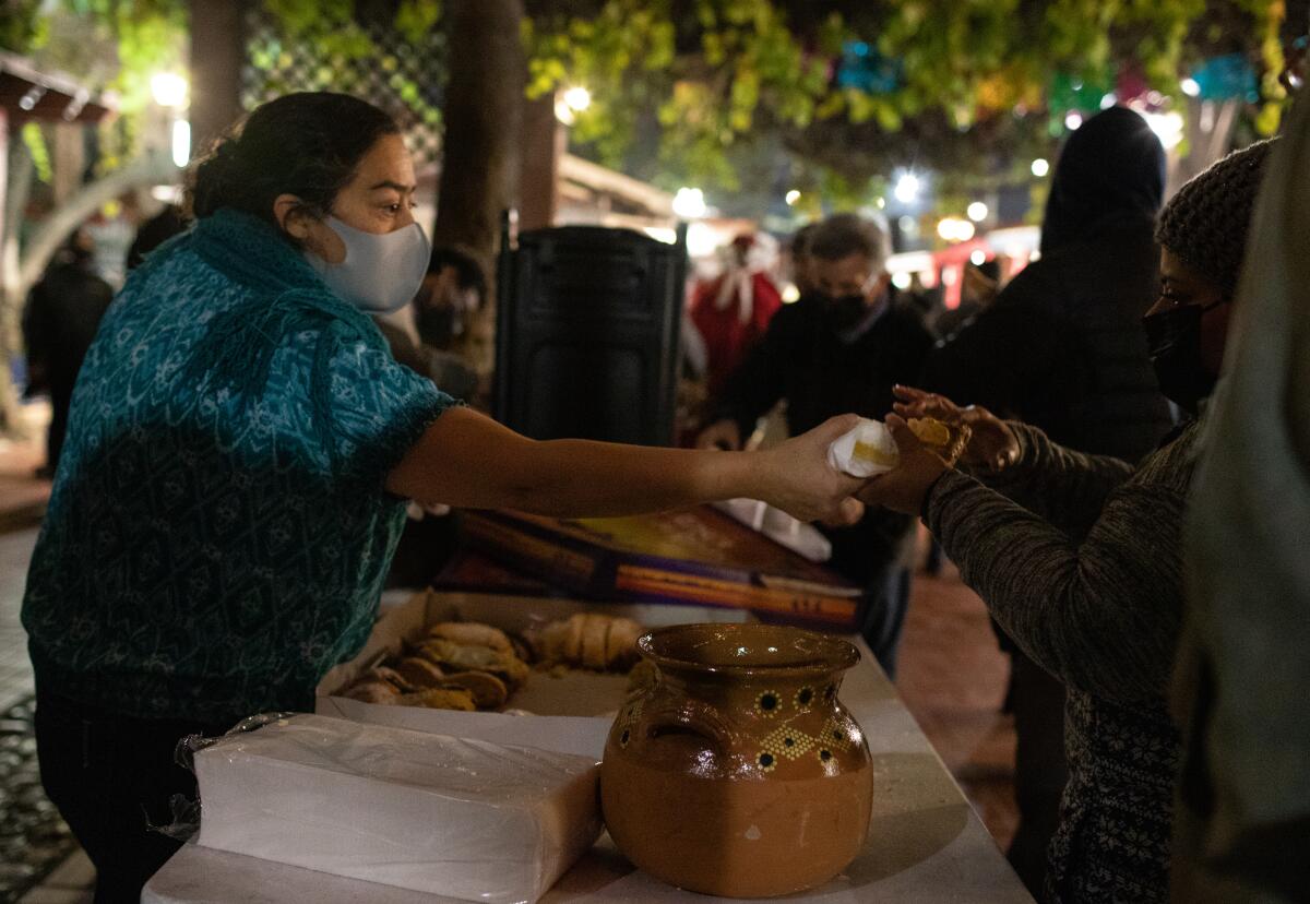 A woman in a mask hands a roll from a box on a table to another person.