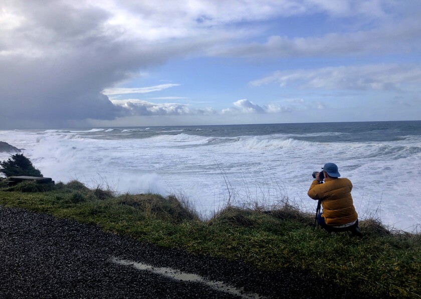 In this Jan. 11, 2020 photo a man photographs waves crashing onto the cliffs at Rodea Point in Lincoln County, Ore. during an extreme high tide that coincided with a big winter storm. Amateur scientists are whipping out their smartphones to document the effects of extreme high tides on shore lines from the United States to New Zealand, and by doing so are helping better predict what rising sea levels due to climate change will mean for coastal communities around the world. (AP Photo/Gillian Flaccus)