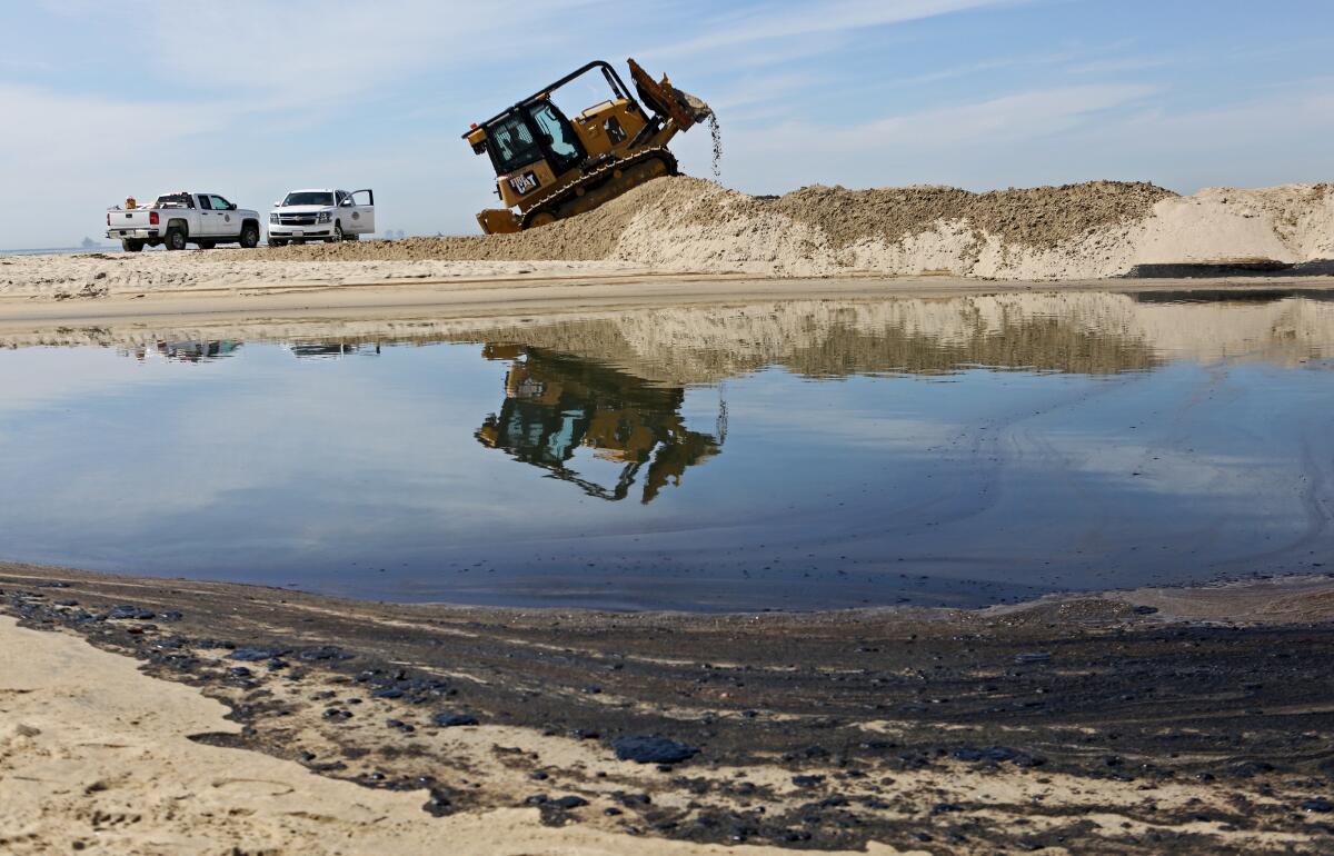 Crude oil covers the sand as a bulldozer creates a berm at the mouth of the Santa Ana river on Sunday.