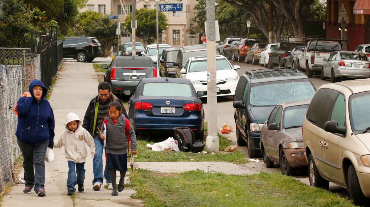 The Hernandez family walks along Miramar Street in Westlake, one neighborhood where a growing number of residents are parking their cars on the strip of land between the sidewalk and the curb.