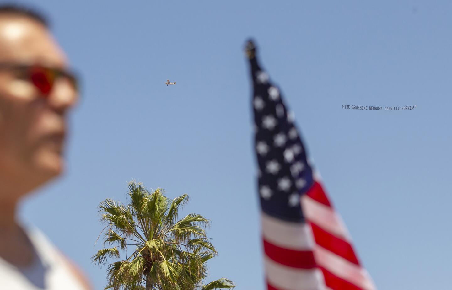 A plane carrying a political message for Gov. Gavin Newsom circles a crowd of protesters in Huntington Beach on Friday.