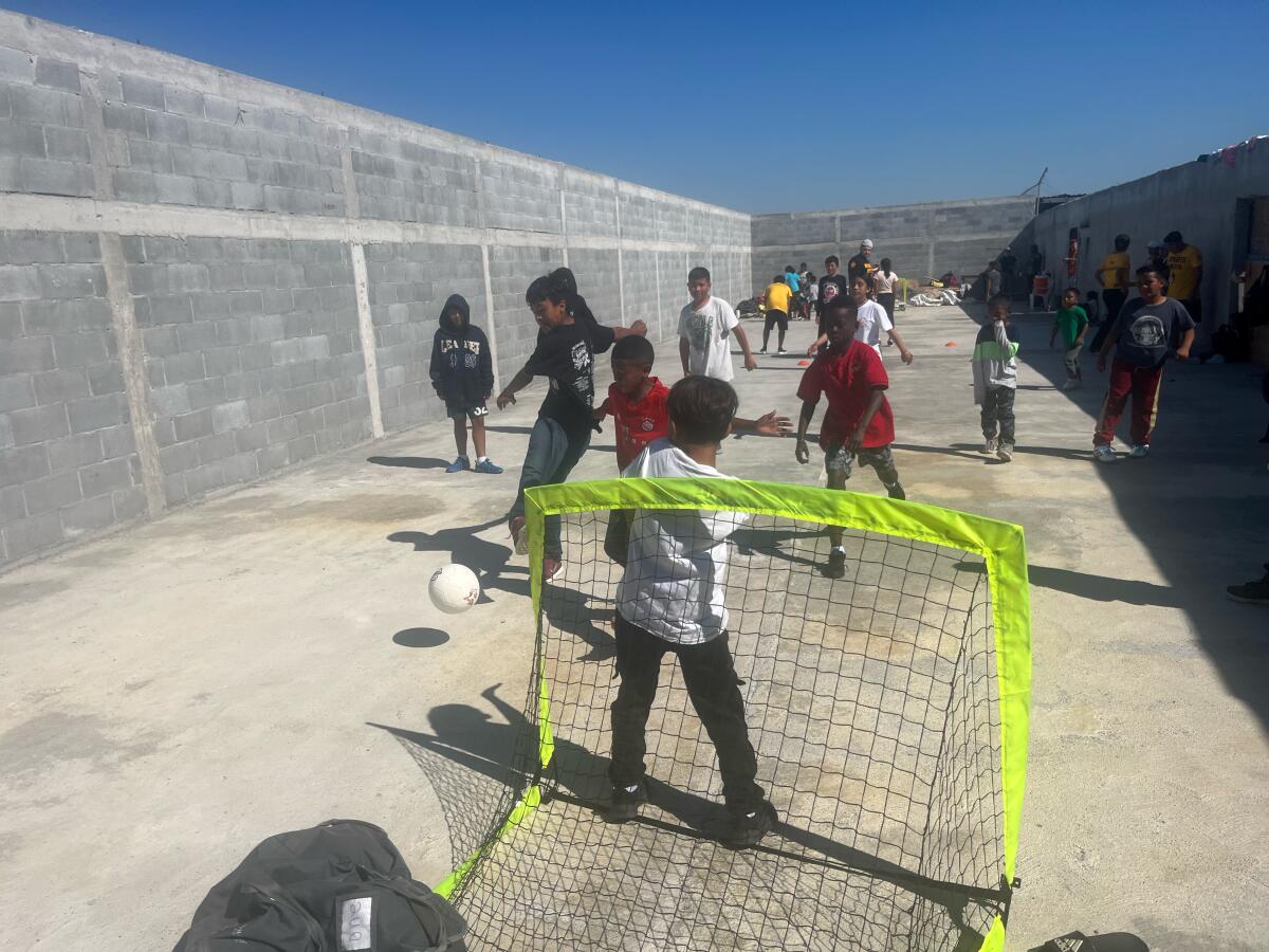 Between concrete walls, children kick a soccer ball. 