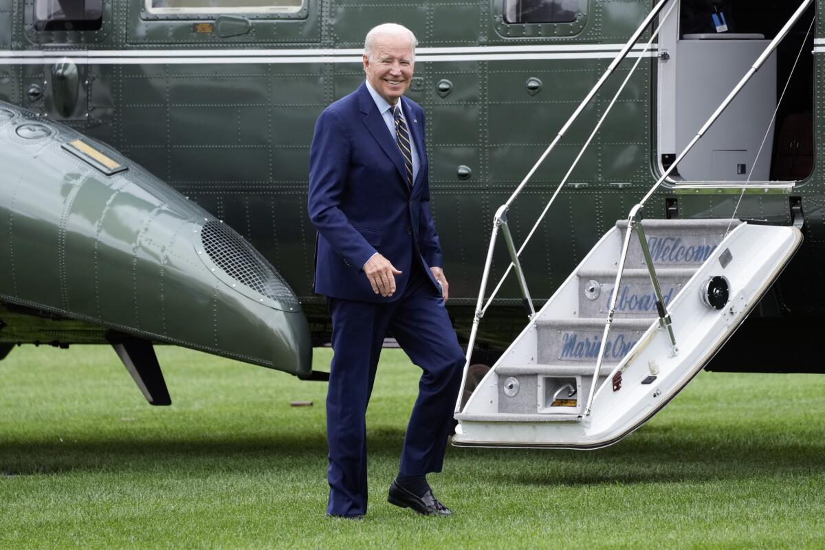 President Biden smiles and walks next to an aircraft.