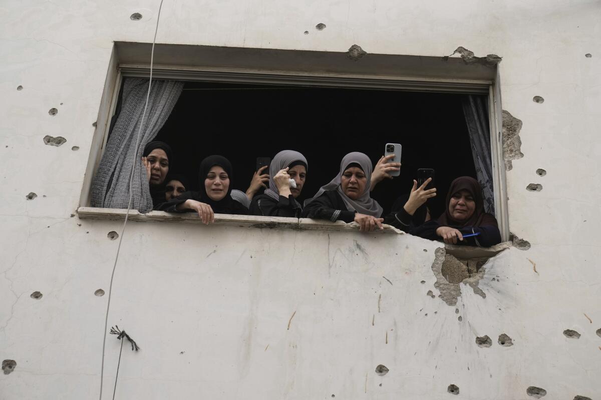 Women look out the window of a building damaged with bullet holes, in Jenin, West Bank.