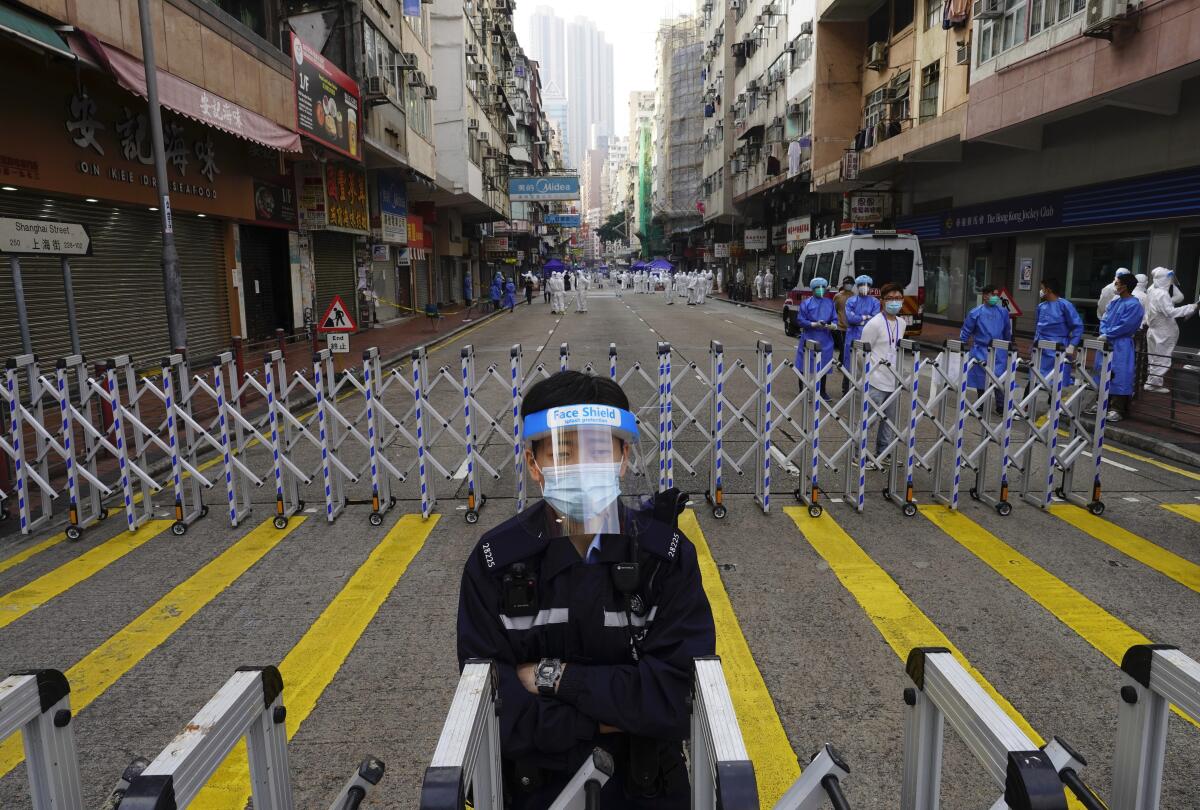 A police officer stands guard in a street in Hong Kong with roadblocks and people in PPE nearby. 