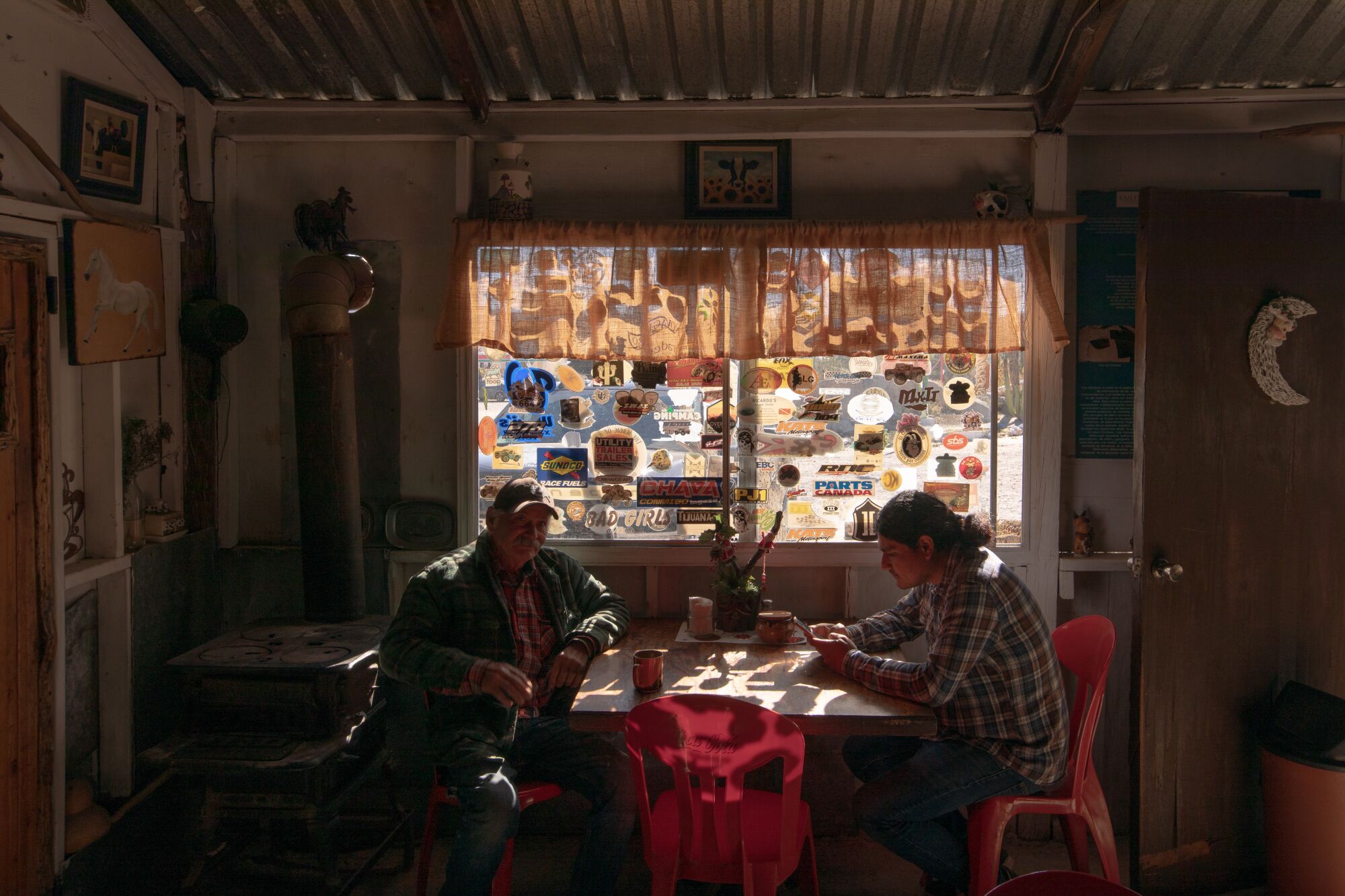 Two people sitting across from each other at a table, illuminated just barely by the sunlight coming in a window above.