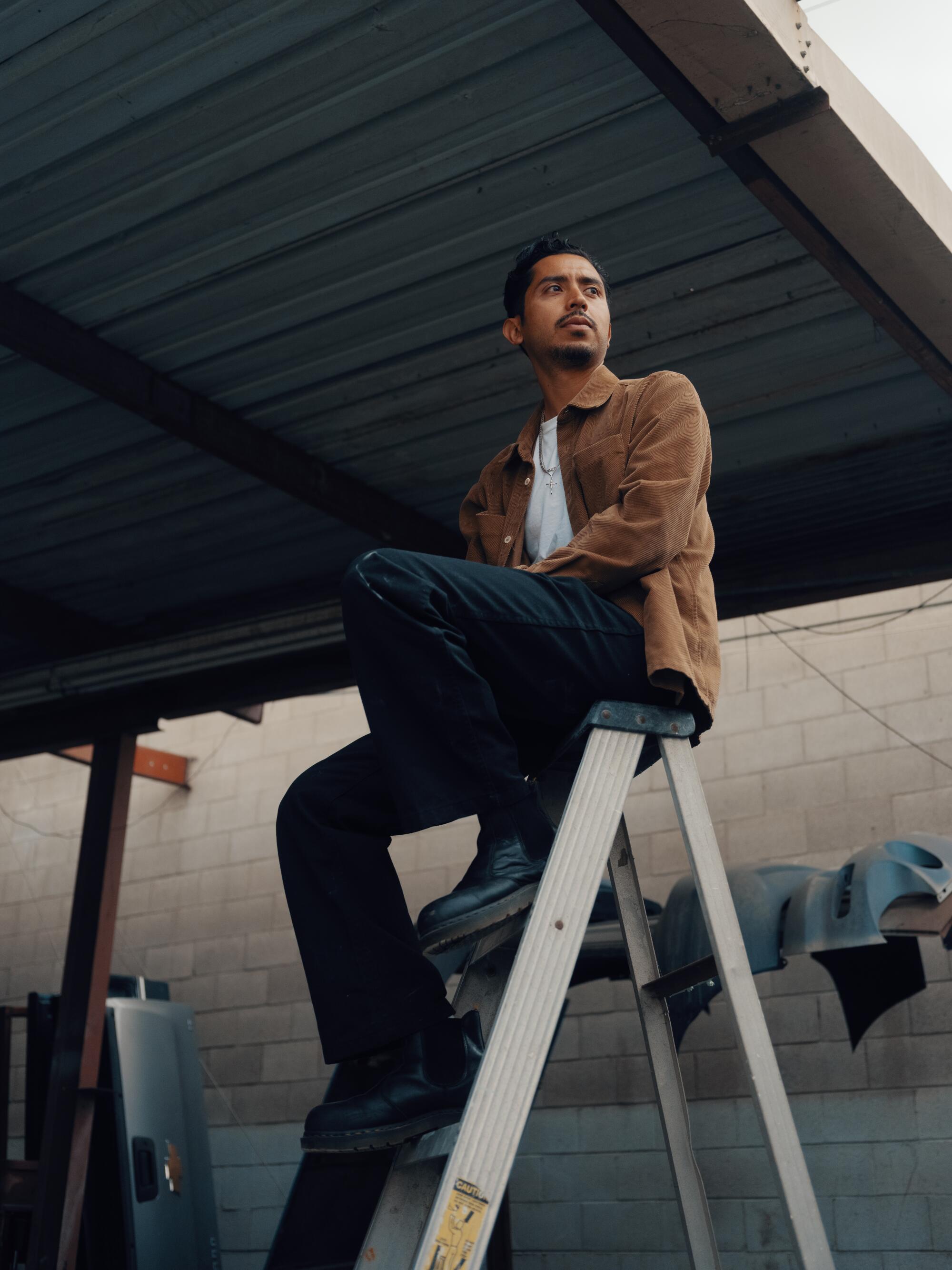 Ryan Preciado sits on a ladder at Jose Auto Body shop in Boyle Heights. 