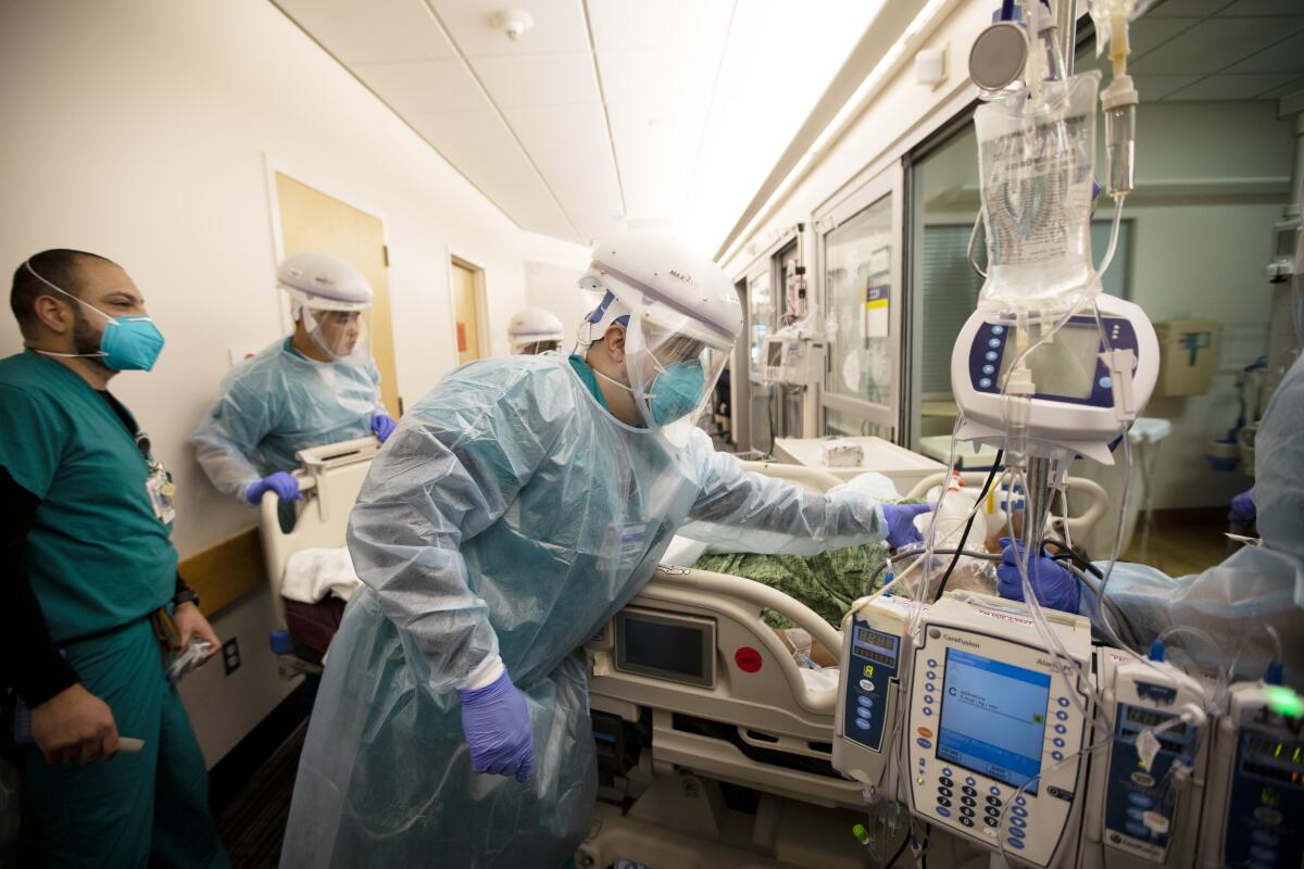 Healthcare workers in full protective gear move a critical patient in a bed through hospital hallway