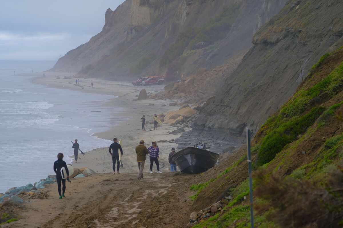 Beachgoers and surfers walk past two pangas that overturned off Black’s Beach on March 11. 