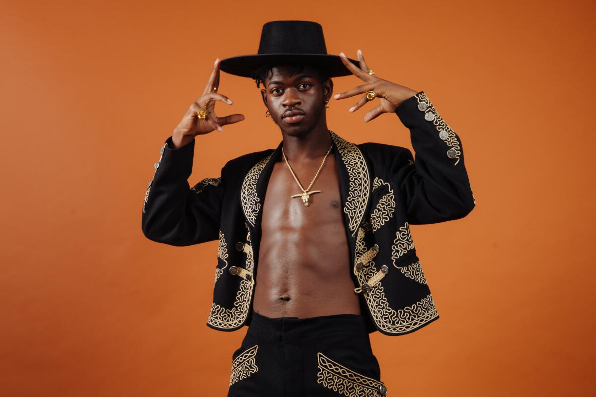 A shirtless man in an embroidered black suit and black hat