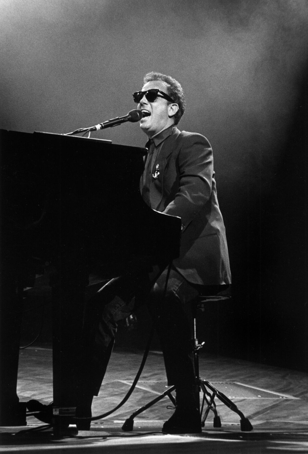 Billy Joel at a piano, wearing dark sunglasses, performing in 1989 New York.