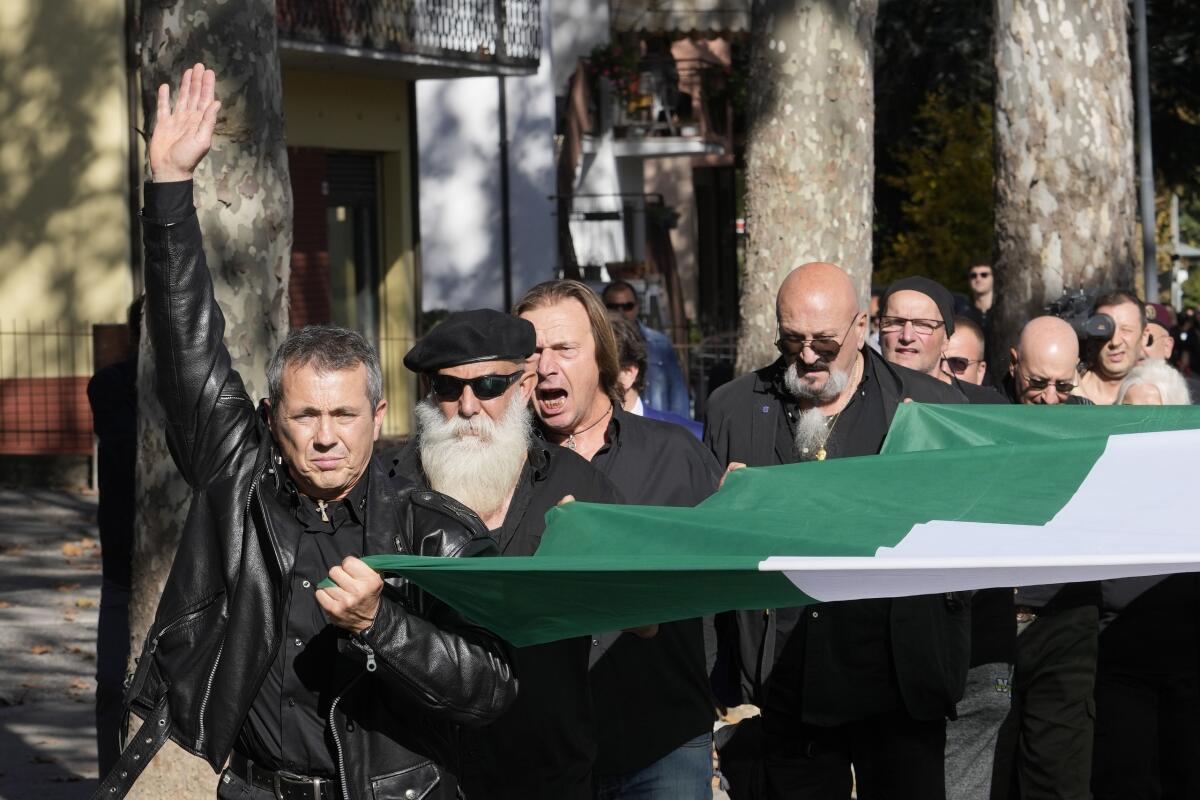 People march in the hometown of former dictator Benito Mussolini while holding a flag.