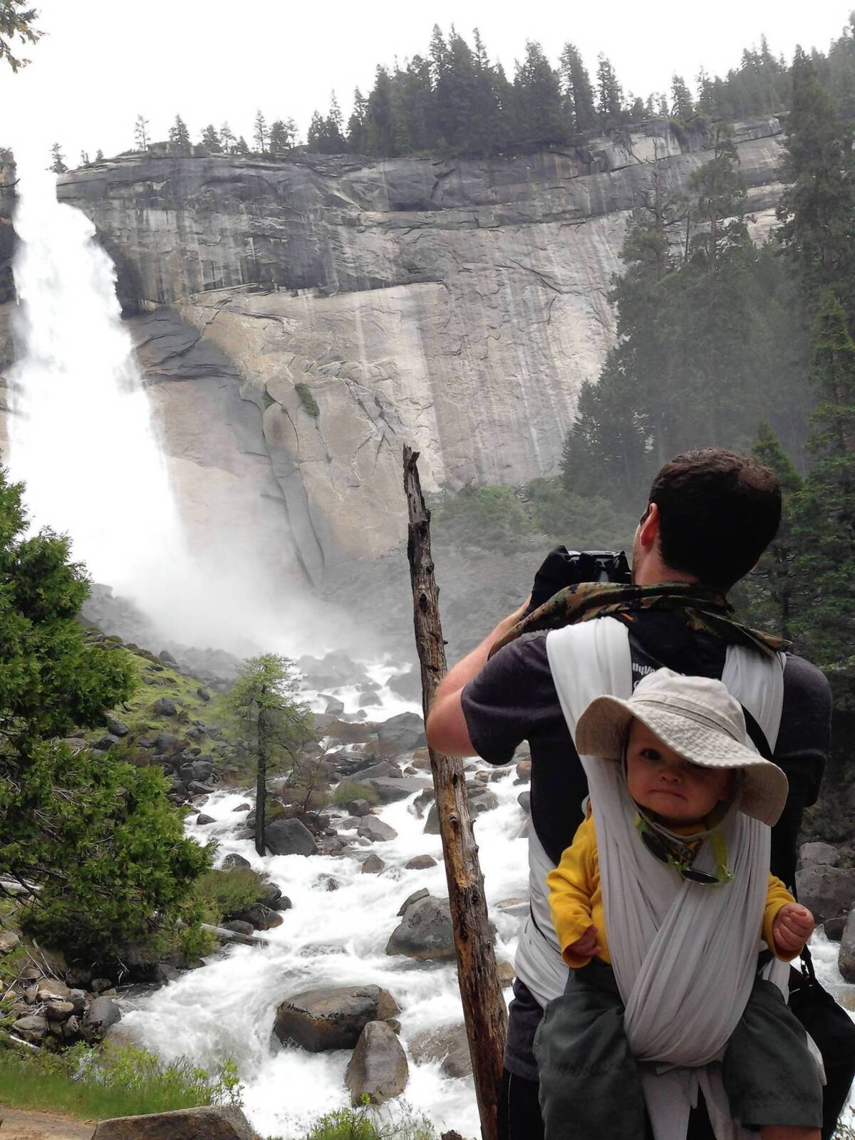 A hiker photographs Nevada Falls along the Mist Trail in Yosemite National Park with a baby on his back.