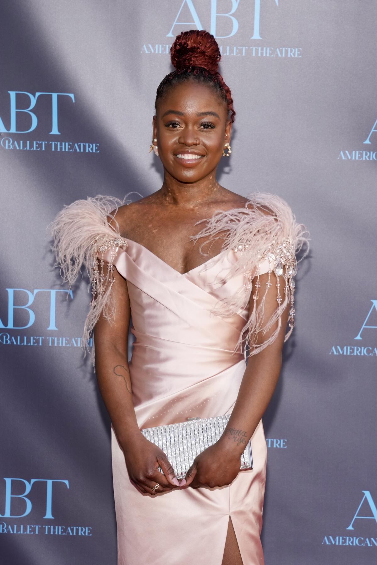 Michaela DePrince smiling in a pale pink gown with feathers on the shoulders