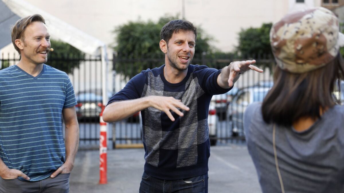 Yuval Sharon, director of "War of the Worlds," works with actors Ross Steeves, left, and Cheryl Umaña Bonilla, right, during a rehearsal in a parking lot along Hill Street in Los Angeles on Nov. 5, 2017.
