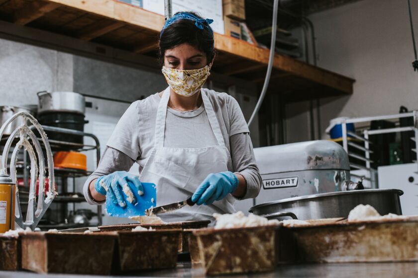 Owner/head baker Roanna Canete uses a mask while baking at her newly opened Gluten Free Baking Co. in North Park. It opened in February just as worries of the pandemic began sweeping through San Diego.