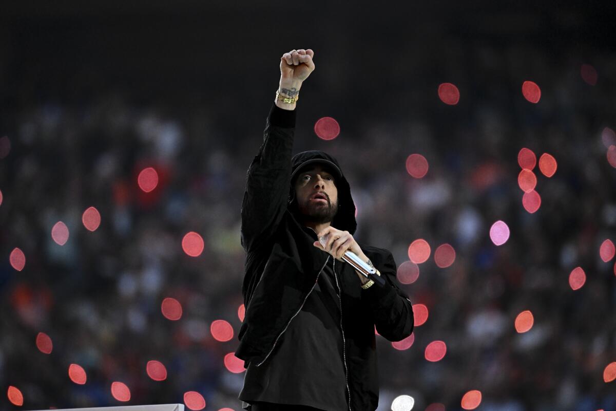 Eminem raises a fist in the air while wearing a black hoodie