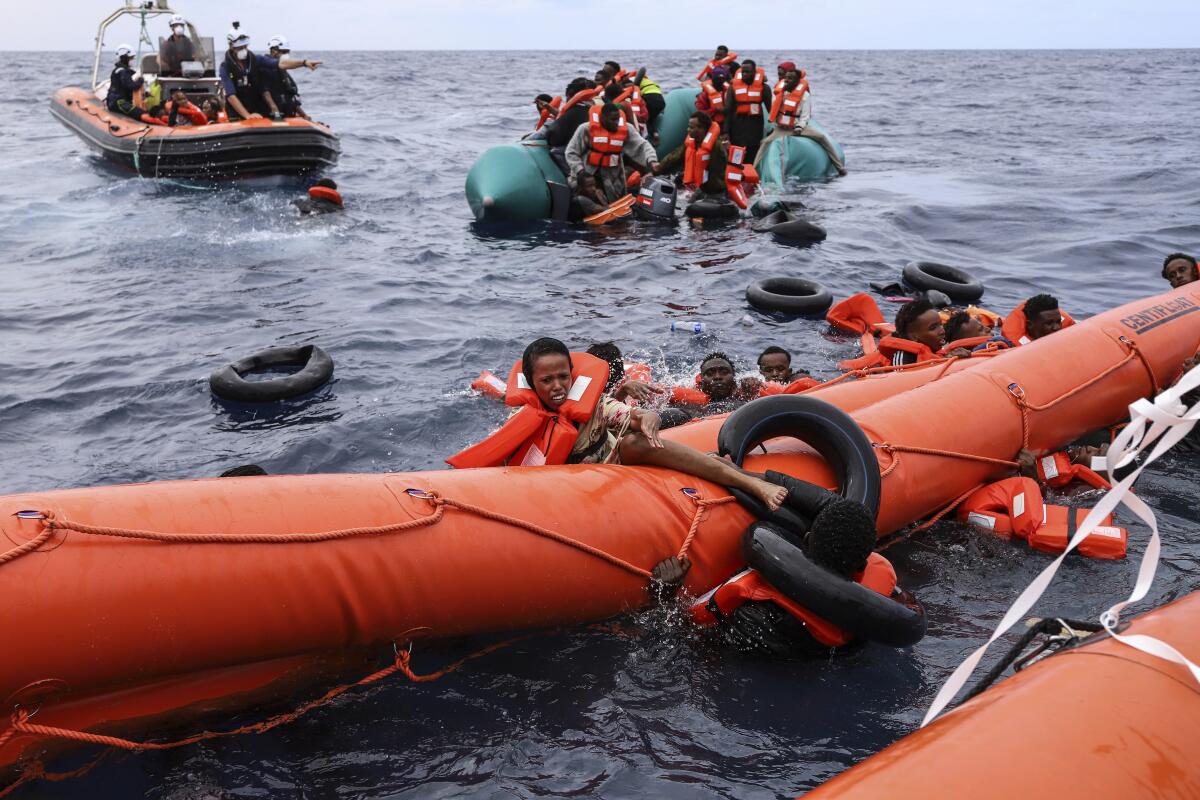 Migrants cling to a floating rubber boom in the water