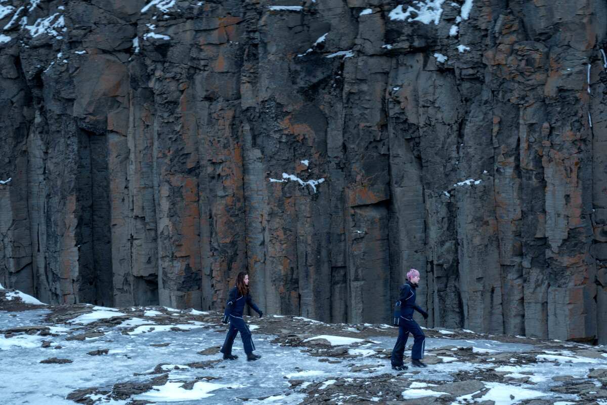 Darby and Sian walk on icy ground next to the walls of a canyon.
