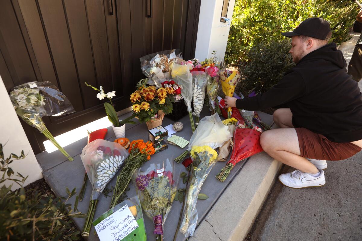 A man crouches next to bouquets at a memorial 