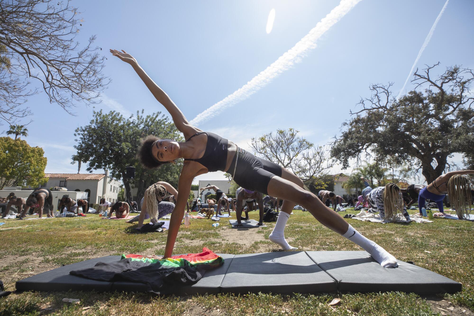 Ivy Coco Maurice raises her left arm to the sky in a yoga pose in a park