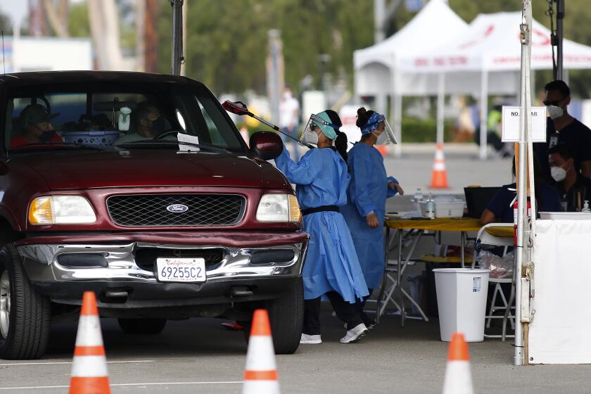 A worker from 360 Clinic passes a COVID-19 self-administering test during a drive-thru testing site on Wednesday morning at the OC Fairgrounds in Costa Mesa.