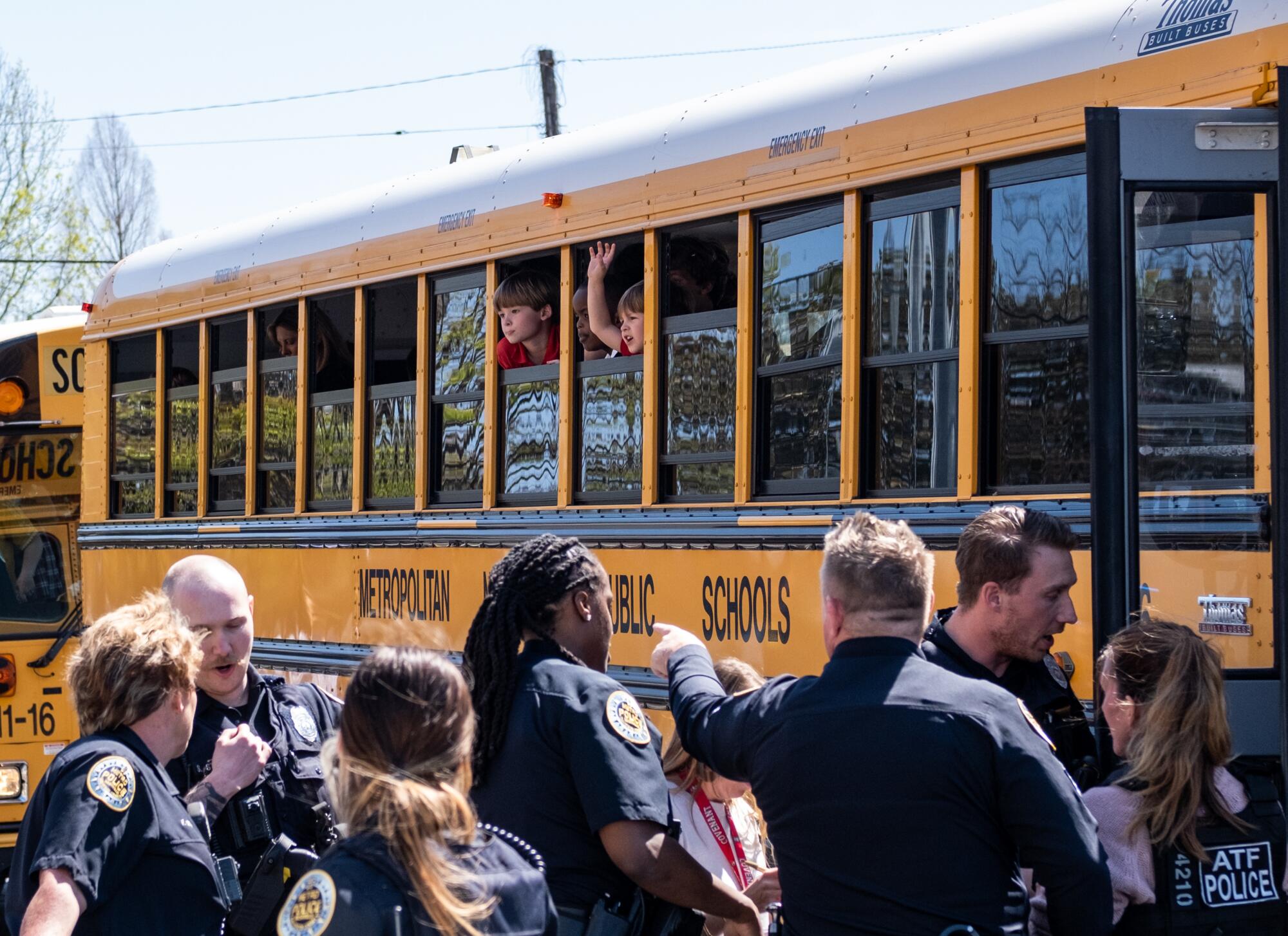 Police officers wait outside a school bus full of children.