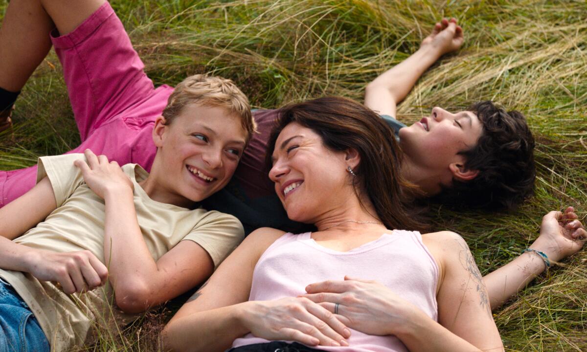 Two young boys and a woman lie in a grassy field.