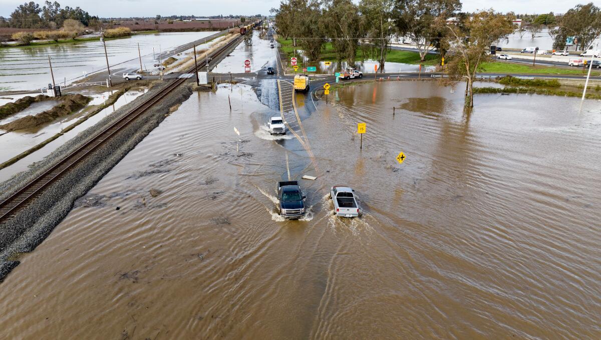 Vehicles drive through standing water on a road.