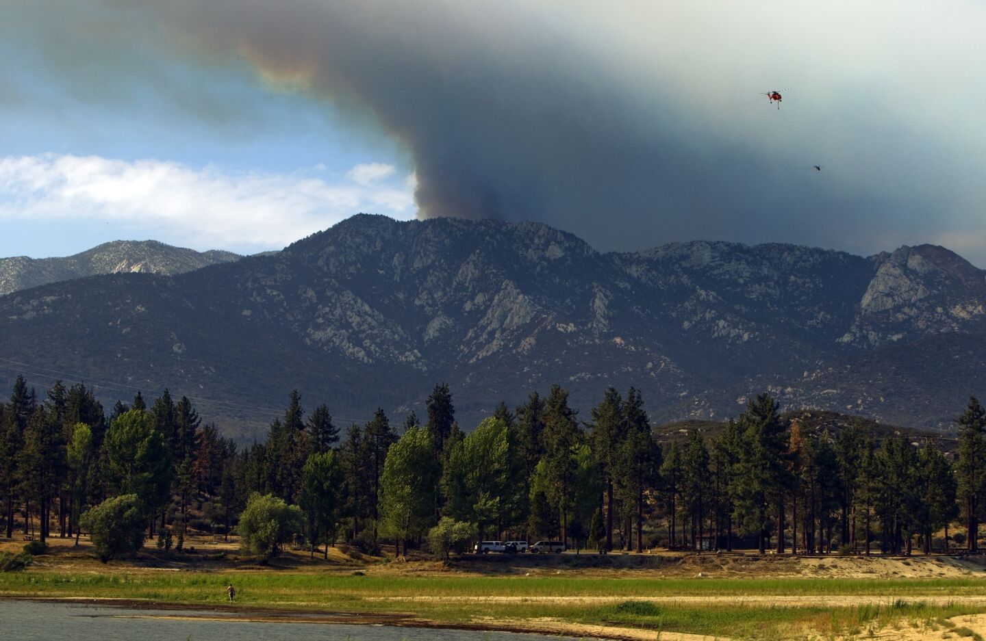 A plume of smoke looms over Lake Hemet as a water-dropping helicopter heads to the lake to refill.
