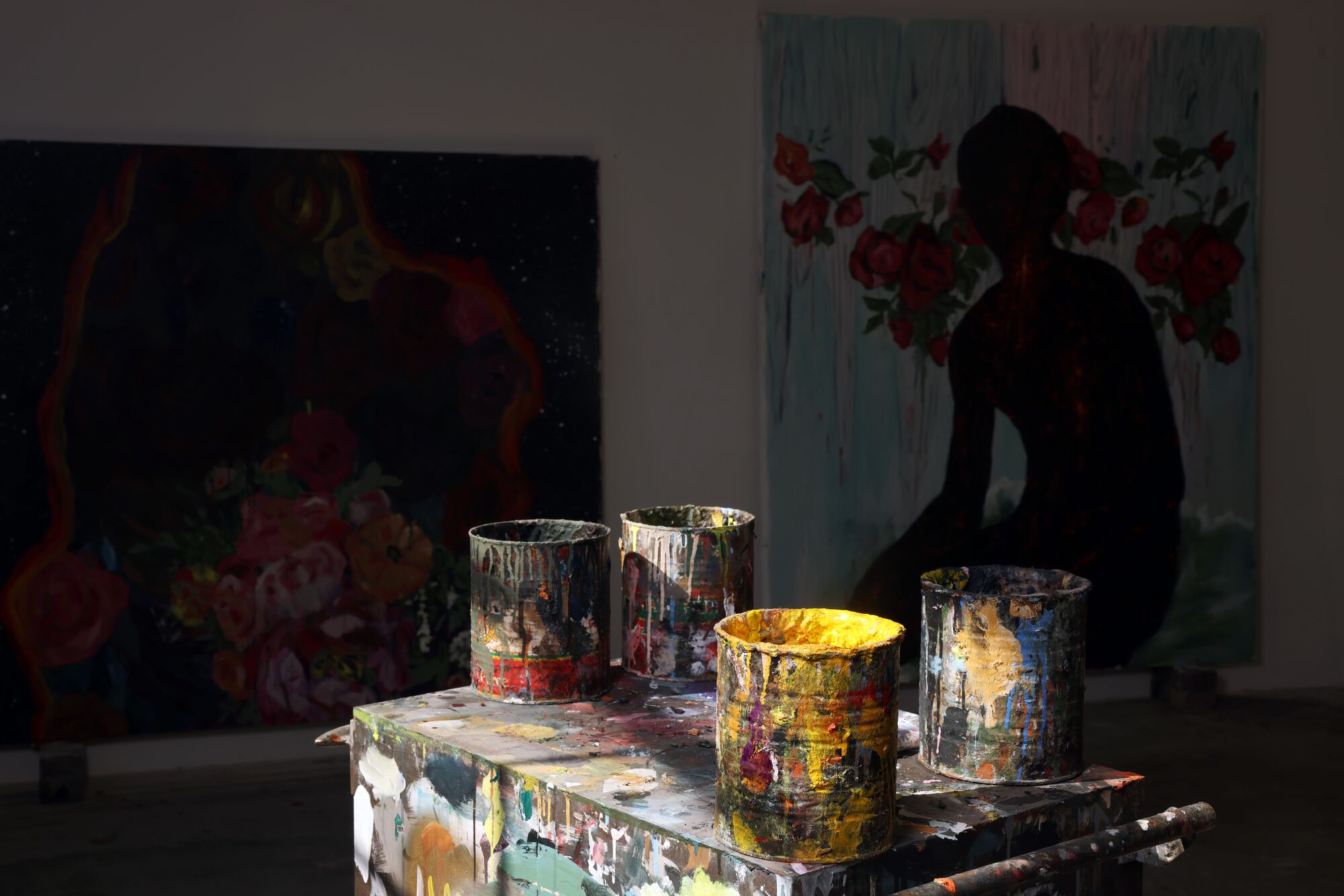 A table with four paint cans covered in paint in front of two paintings