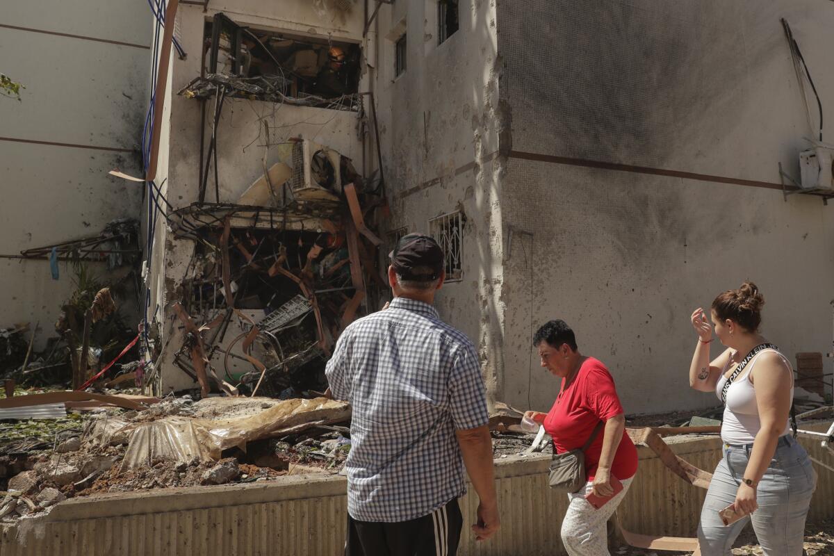 Three people walk amid the rubble of a residential building hit by rocket fire 