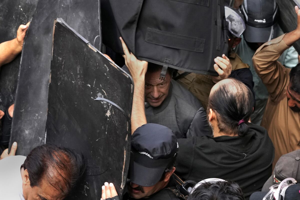 Security personnel hold bulletproof shields to secure former Prime Minister Imran Khan, center, after appearing in a court, in Lahore, Pakistan, Tuesday, March 21, 2023. A Pakistani court on Tuesday granted Khan a weeklong bail in two cases in which he faces terrorism charges, officials said. The ruling gave the embattled ousted premier and now popular opposition leader another brief reprieve from arrest. (AP Photo/K.M. Chaudary)