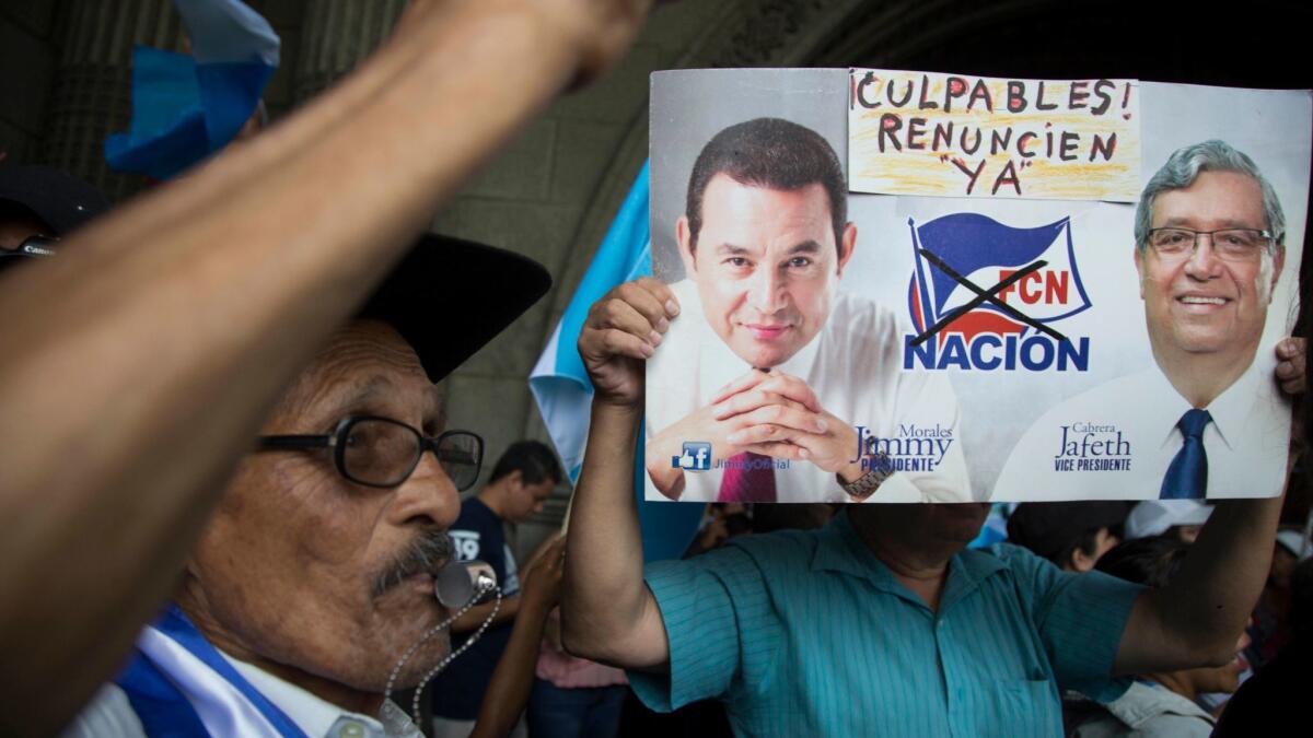 A demonstrator holds a sign with images of Guatemala's President Jimmy Morales, left, and his Vice President Jafeth Cabrera that reads: "Guilty! Resign now!" during a protest outside the National Palace of Culture in Guatemala City on Aug. 27, 2017.