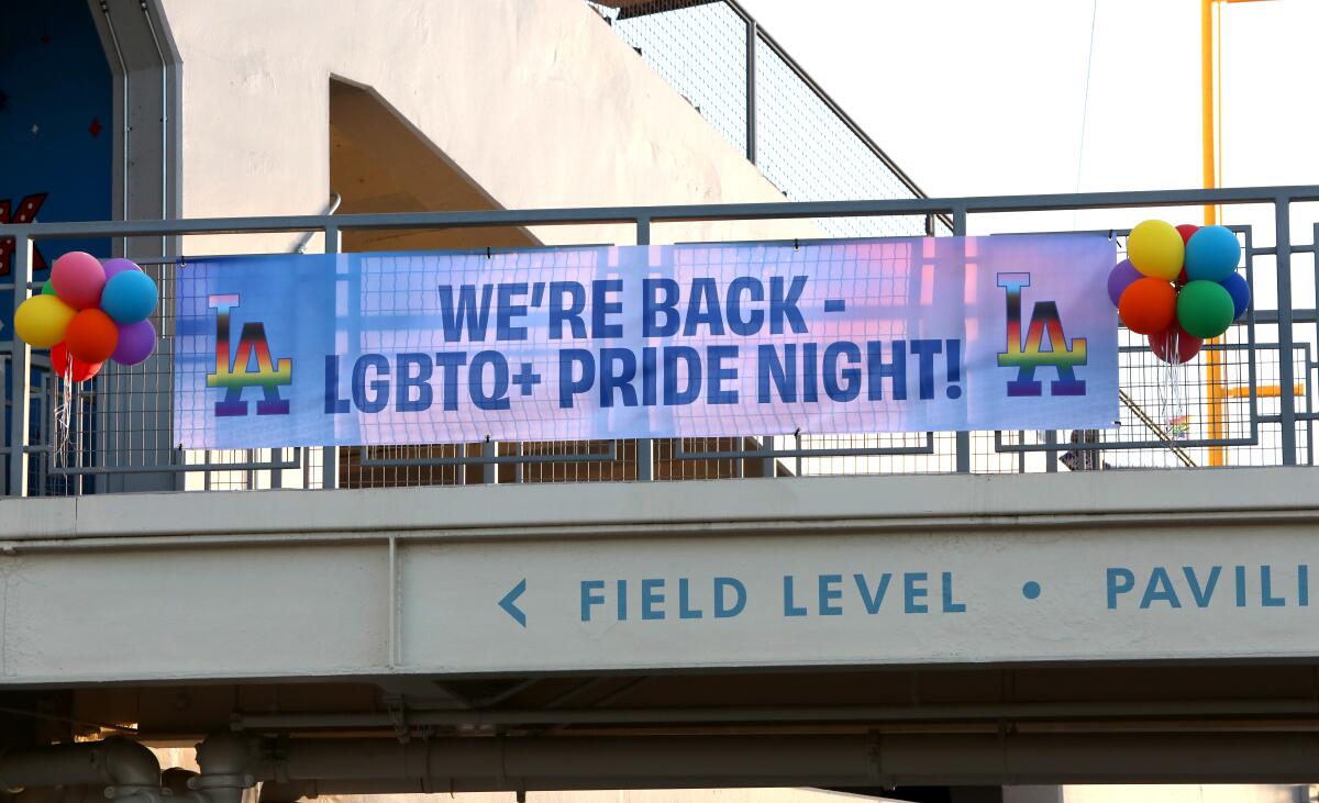 A banner hanging from a railing reads, "We're back — LGBTQ+ Pride Night!" with the Dodgers' "LA" logo in rainbow colors