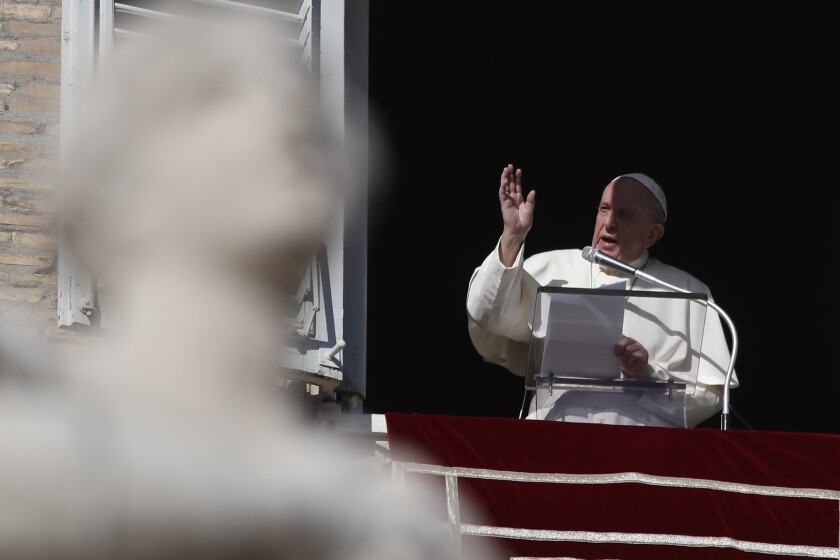 Pope Francis, holding papers and speaking into a microphone, speaks and gestures to the crowd from a window.