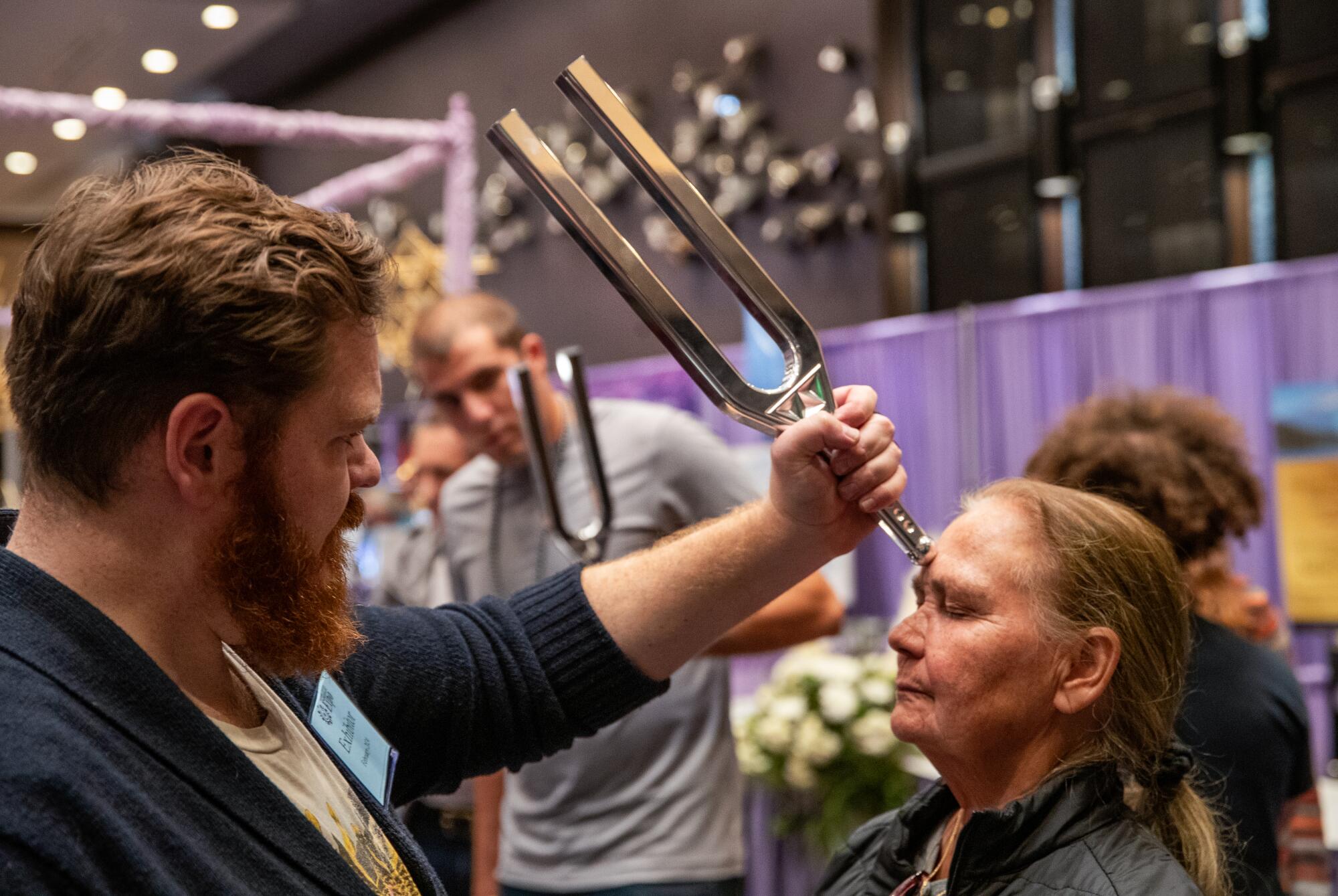 Eric Villhauer holds a giant tuning fork used as a sound therapy tool on the forehead of Denise Visco.
