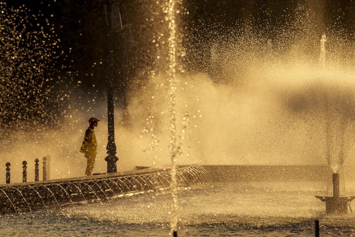 A figure is silhouetted next to a fountain of water.