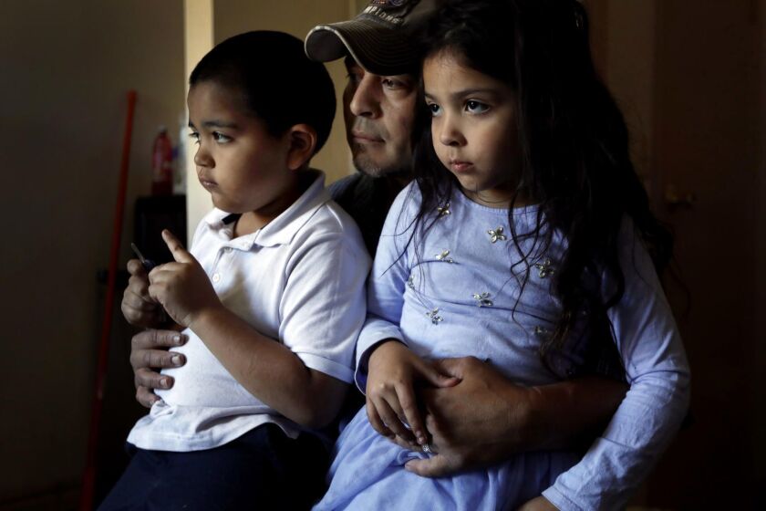 PACOIMA, CA OCTOBER 16, 2018: Marcos, 7, left, and Kimberly, 5, right sits on their father Jose's lap, middle, as they listen during a Los Angeles Times interview at a motel in Pacoima, CA October 4, 2018. Their family is currently staying in a motel operated by LA Family Housing. (Francine Orr/ Los Angeles Times)
