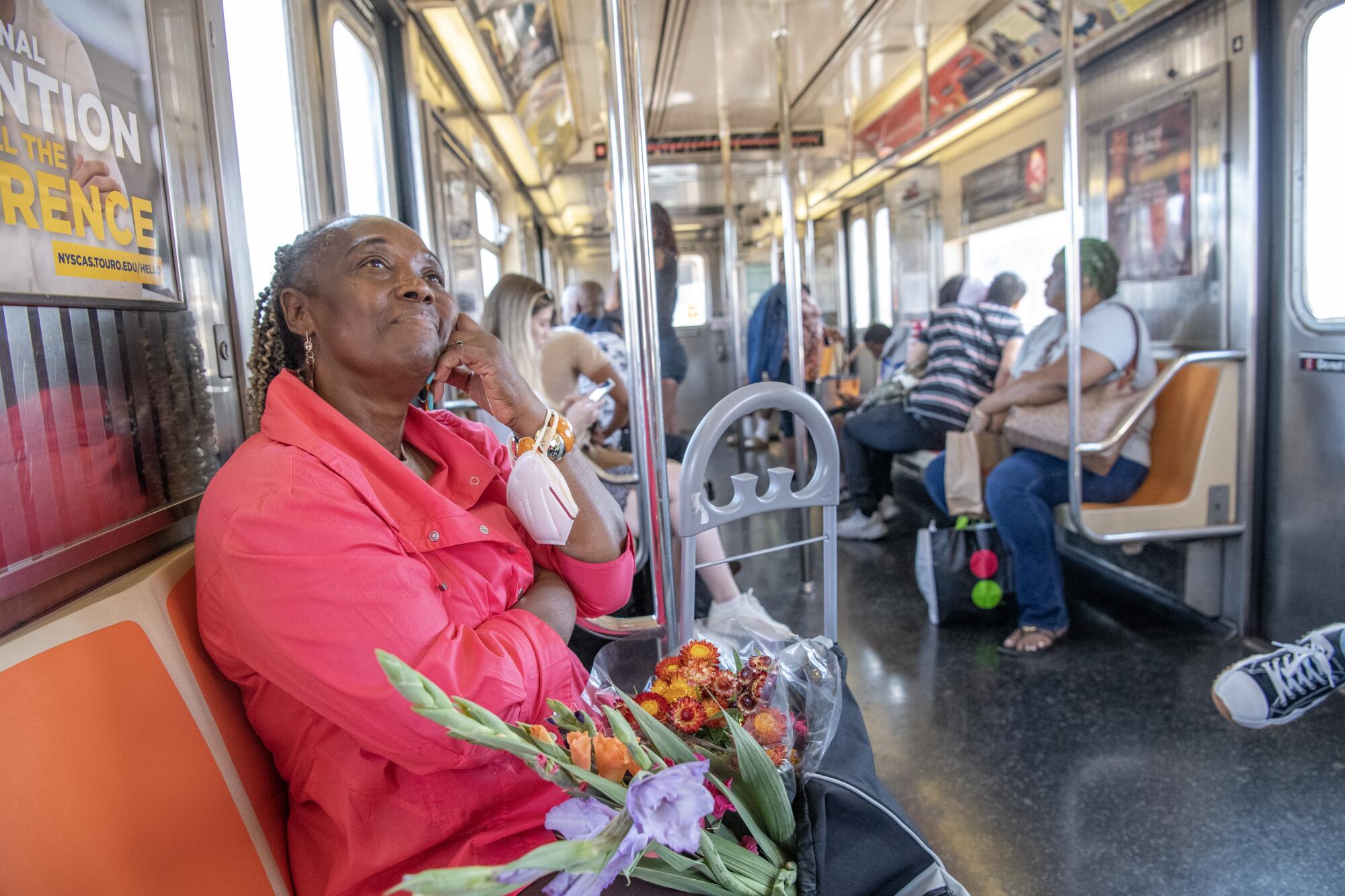 A woman looking up from her seat on a subway, a variety of fresh flowers in her cart