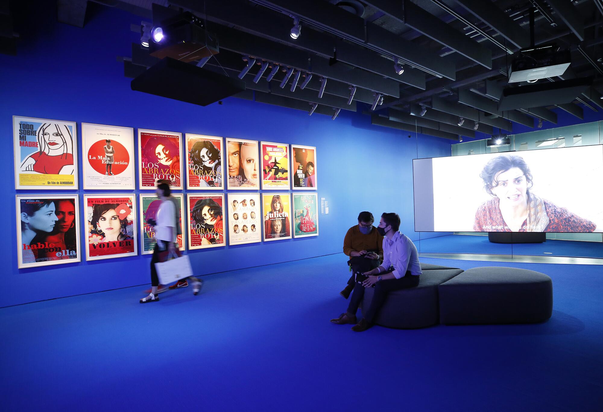 Visitors look at a wall of posters from movies made by Pedro Almodóvar.