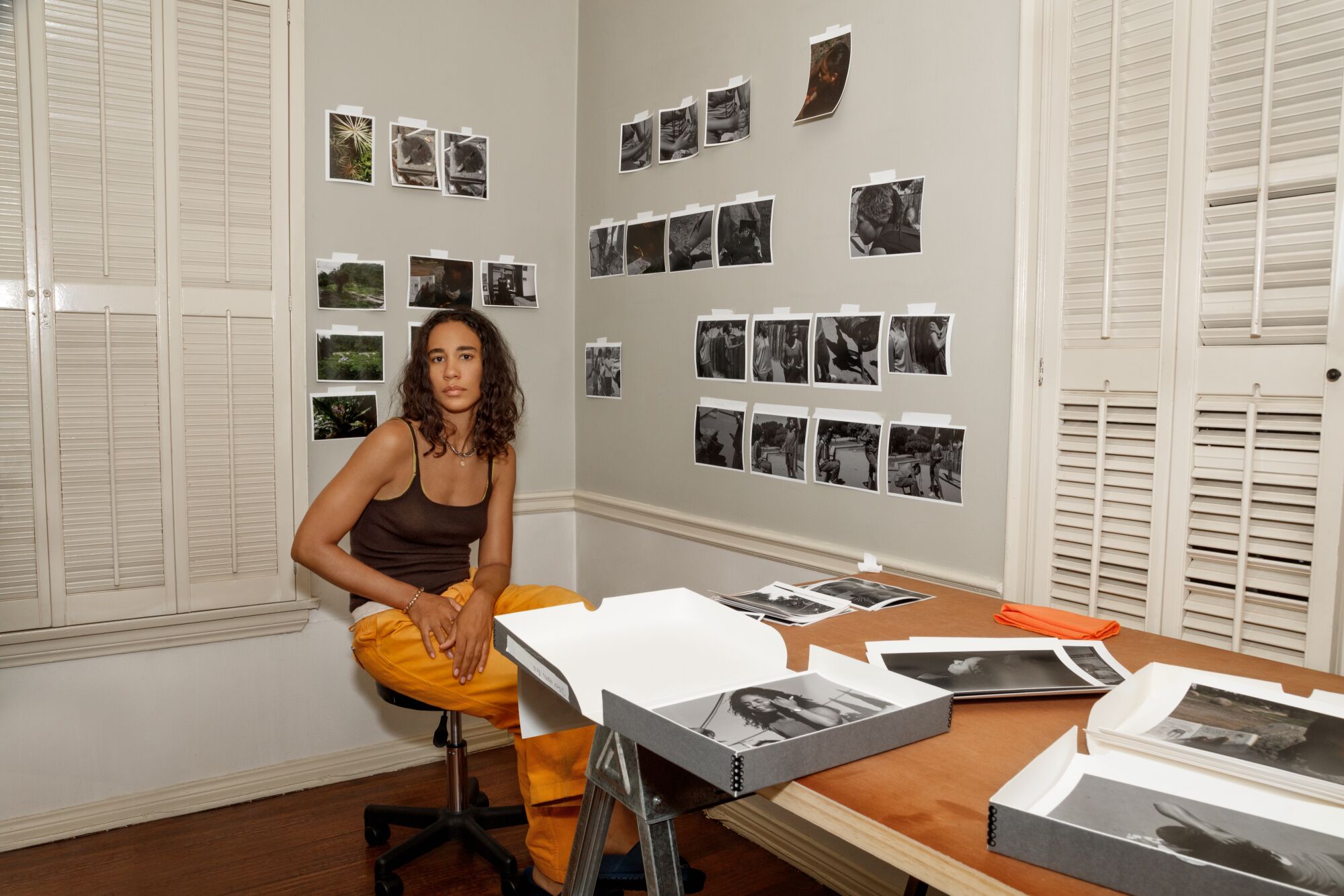 Lacey Lennon sitting in her studio in front of photographs hanging on the wall behind her and stacked on a table next to her.