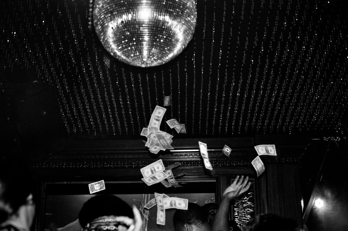 A disco ball hangs from the ceiling and dollar bills fly in the air 